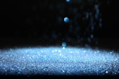 Shiny blue glitter falling down on black background. Bokeh effect