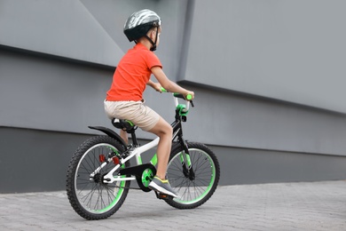 Photo of Little boy riding bicycle on street near gray wall