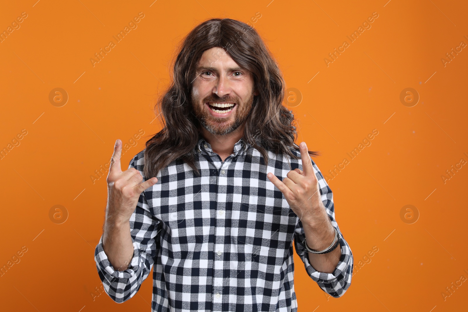 Photo of Hippie man showing rock gesture on orange background