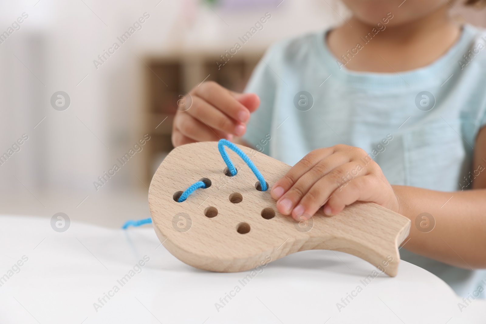 Photo of Motor skills development. Little girl playing with wooden lacing toy at table indoors, closeup