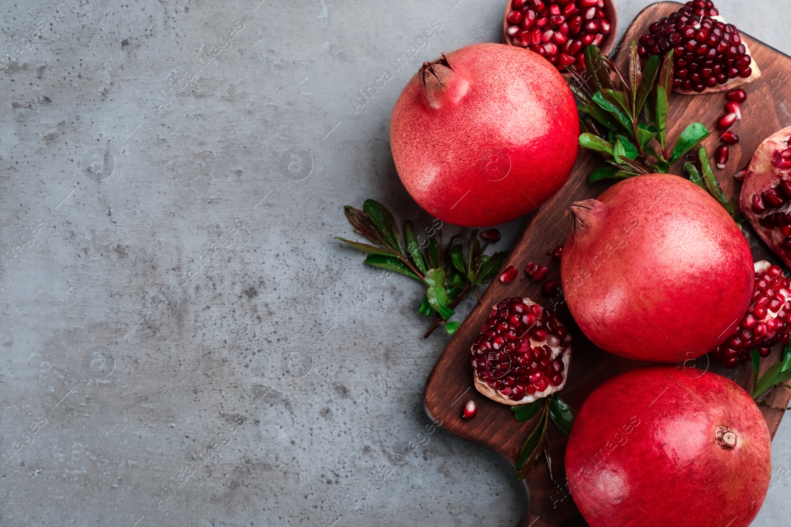 Photo of Delicious ripe pomegranates on grey table, flat lay. Space for text