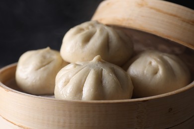 Photo of Delicious bao buns (baozi) in bamboo steamer on black background, closeup