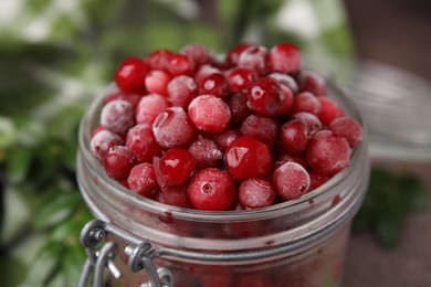 Photo of Frozen red cranberries in glass jar on table, closeup