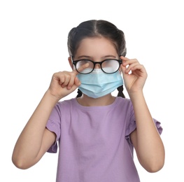 Little girl wiping foggy glasses caused by wearing medical face mask on white background. Protective measure during coronavirus pandemic