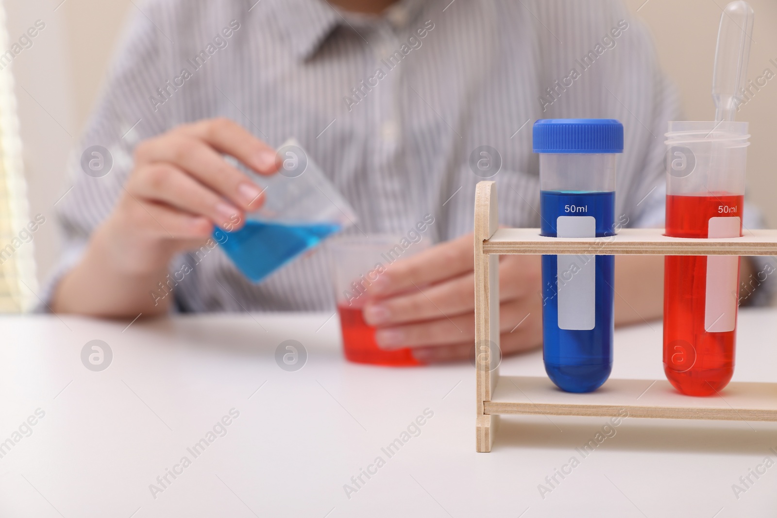 Photo of Girl mixing colorful liquids at white table indoors, selective focus. Kids chemical experiment set