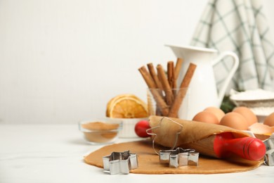 Photo of Dough, rolling pin and cookie cutters on white table, space for text. Christmas biscuits