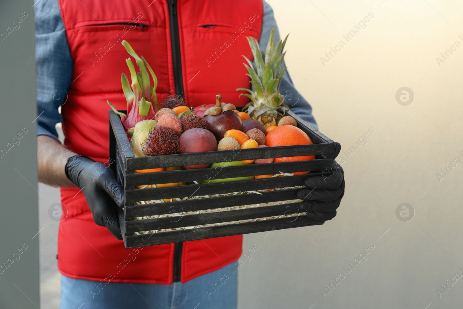 Photo of Courier holding crate with assortment of exotic fruits outdoors, closeup