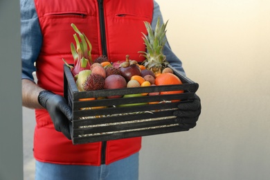 Courier holding crate with assortment of exotic fruits outdoors, closeup