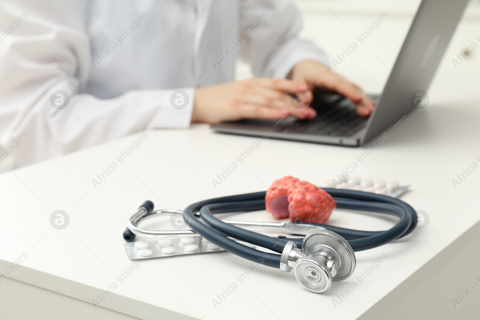 Photo of Endocrinologist working at table, focus on stethoscope and model of thyroid gland