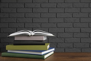 Photo of Stack of hardcover books on wooden table near dark brick wall, space for text