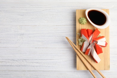 Photo of Fresh crab sticks with soy sauce served on white wooden table, top view. Space for text