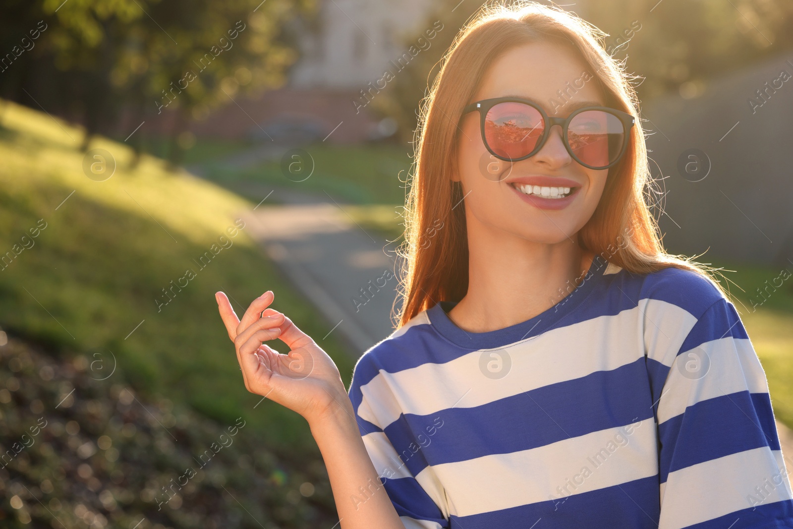 Photo of Beautiful smiling woman wearing sunglasses in park, space for text