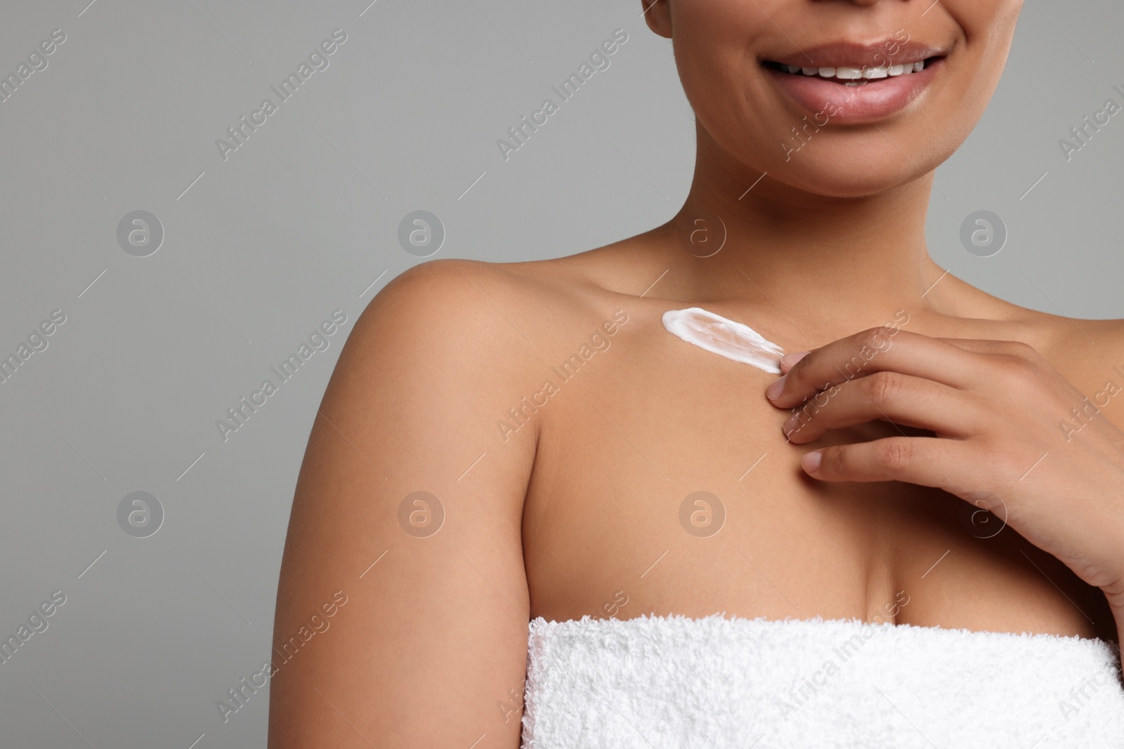 Photo of Young woman applying cream onto body on grey background, closeup. Space for text