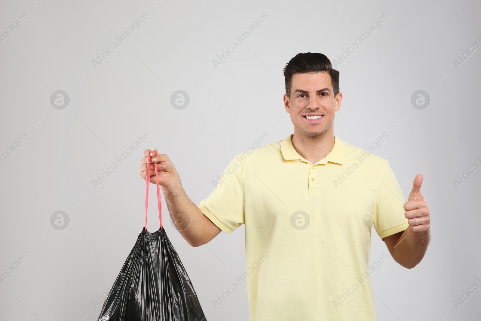 Photo of Man holding full garbage bag on light background