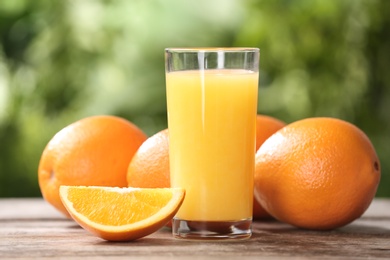 Glass of fresh juice and oranges on wooden table