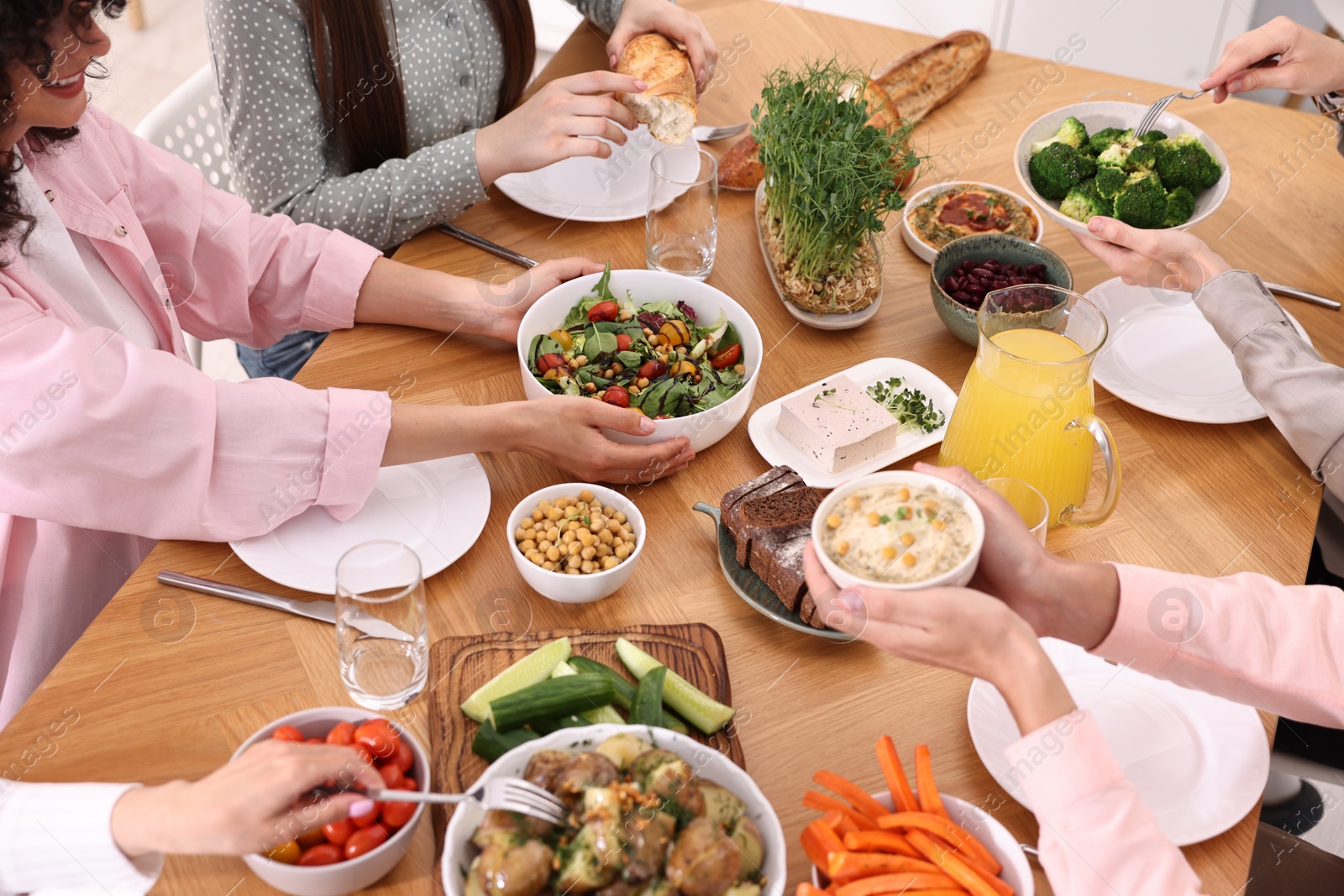 Photo of Friends eating vegetarian food at wooden table indoors, closeup