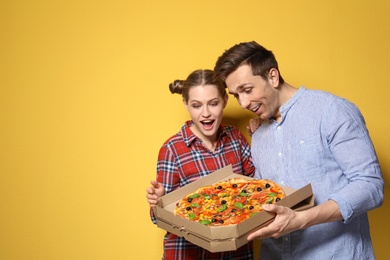 Attractive young couple with delicious pizza on color background