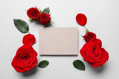 Photo of Blank card, beautiful red roses and petals on light background, flat lay. Space for text