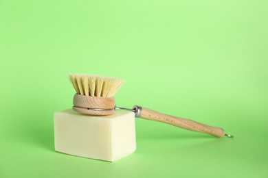 Photo of Cleaning brush and soap bar on green background. Dish washing supplies