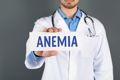 Doctor holding sign with word ANEMIA on grey background, closeup
