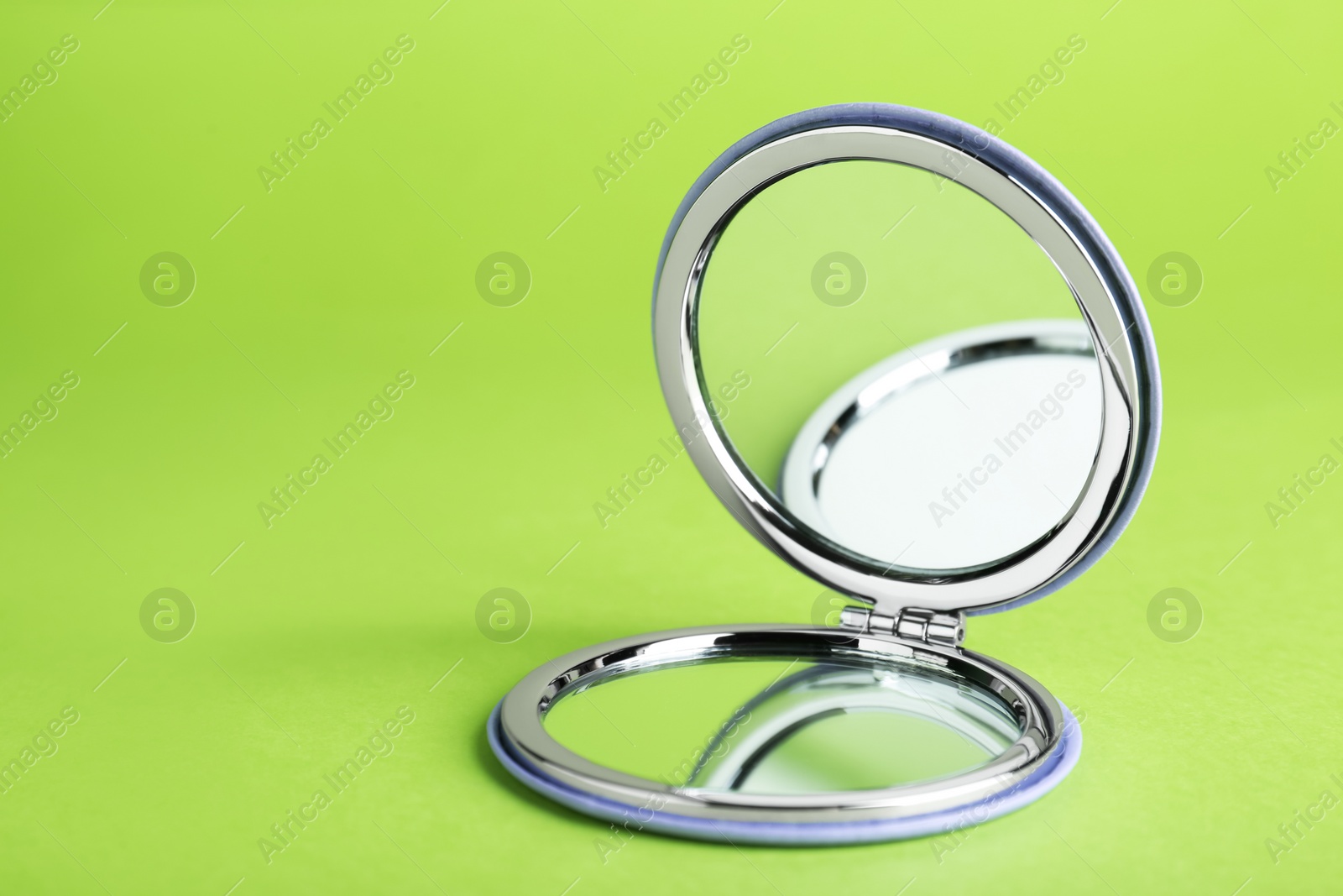 Photo of Stylish cosmetic pocket mirror on light green background. Space for text