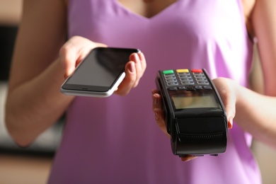 Woman using modern payment terminal with mobile phone indoors, closeup
