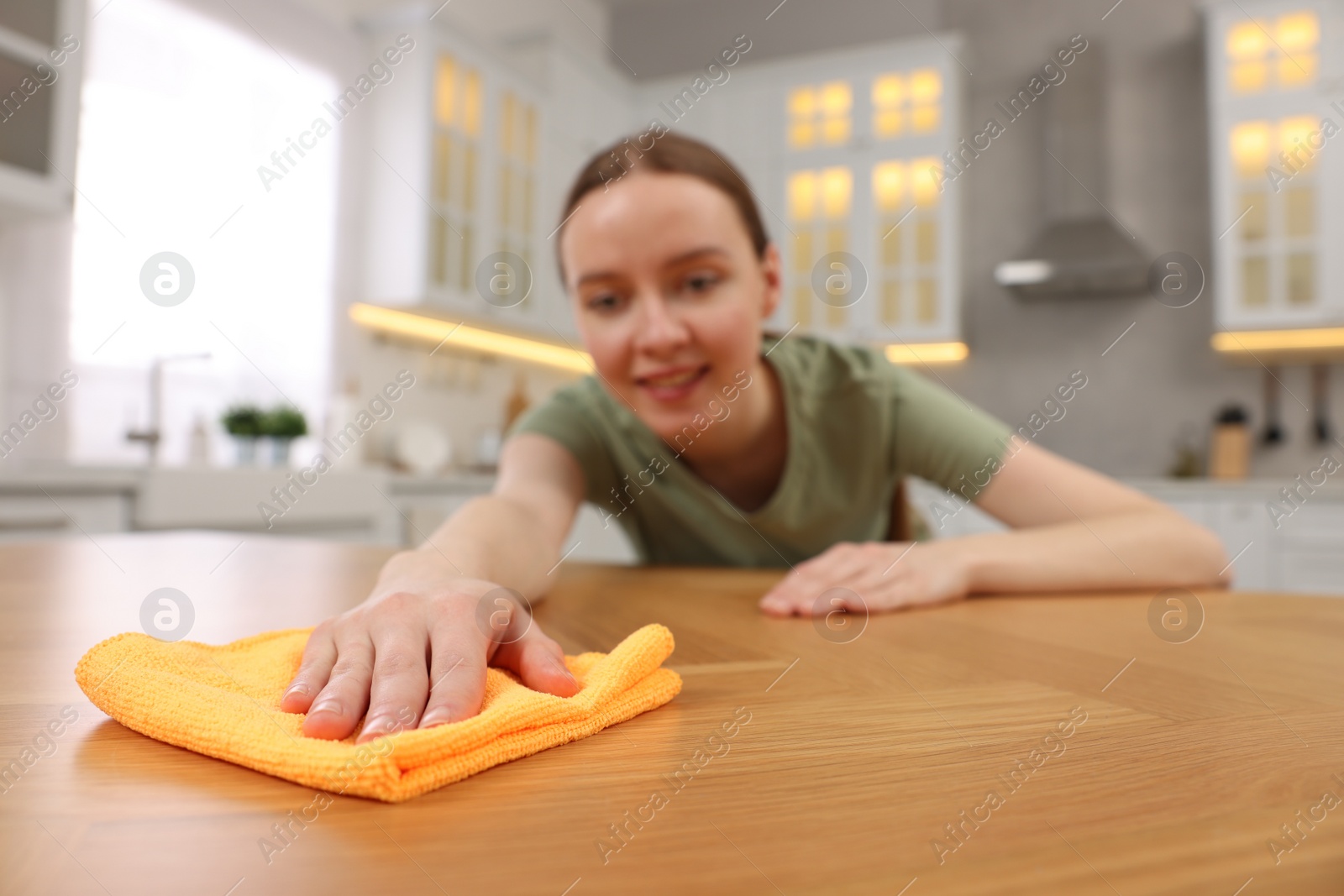 Photo of Woman with microfiber cloth cleaning wooden table in kitchen, selective focus