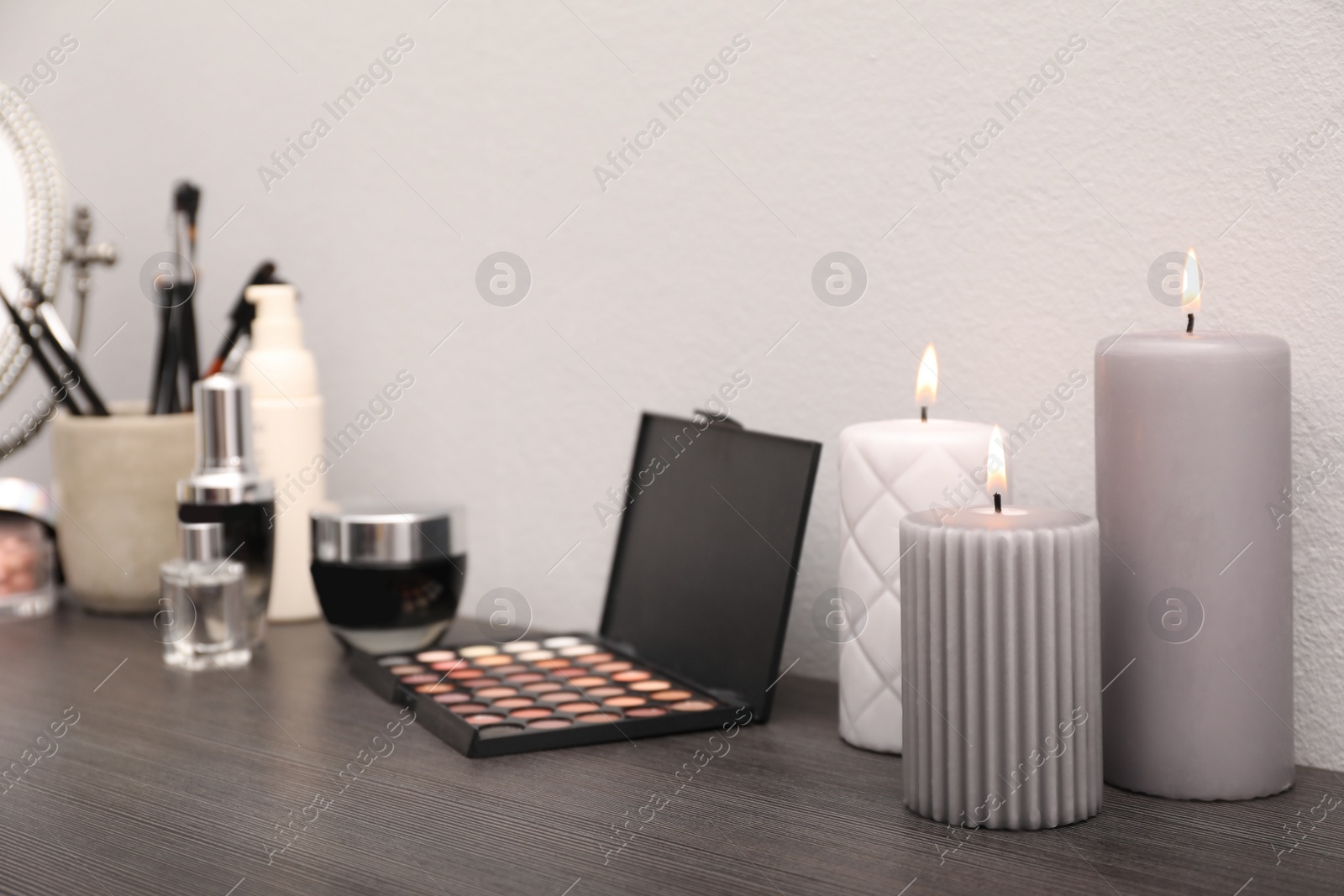 Photo of Mirror, candles and different makeup products on dark wooden dressing table near wall