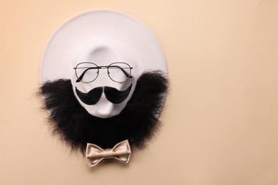 Photo of Man's face made of artificial mustache, beard and glasses on beige background, top view. Space for text