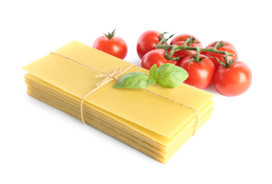 Uncooked lasagna sheets, tomatoes and basil on white background