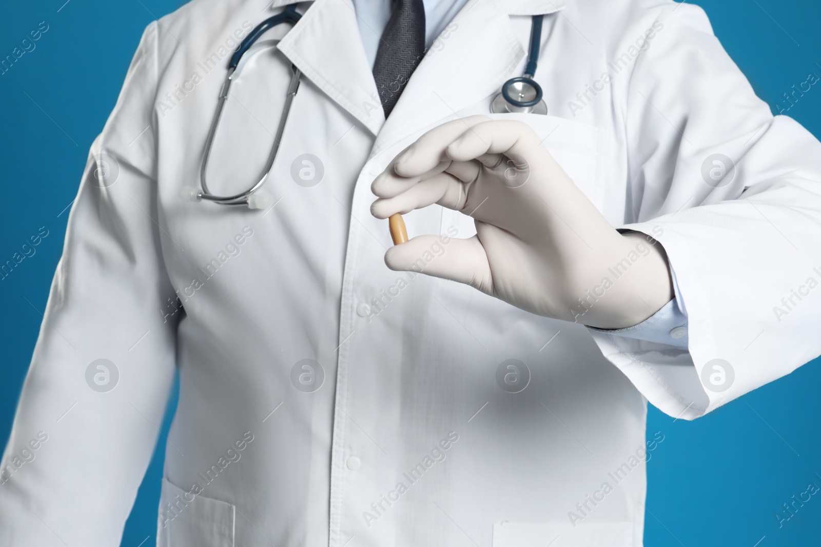 Photo of Doctor holding suppository for hemorrhoid treatment on blue background, closeup