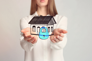 Home security concept. Woman holding house on light background, closeup