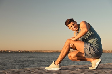 Photo of Man in sportswear having knee problems near river at sunset