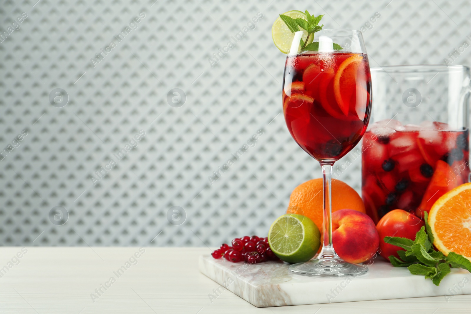 Photo of Glass and jug of Red Sangria with fruits on white wooden table, space for text