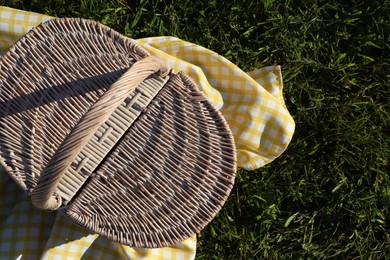 Photo of Picnic basket with checkered tablecloth on green grass, top view. Space for text