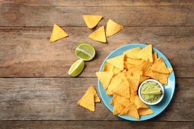 Photo of Plate with delicious mexican nachos chips, guacamole sauce and lime on wooden table, flat lay. Space for text