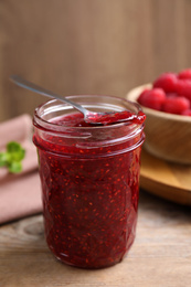 Photo of Delicious raspberry jam in jar on wooden table, closeup