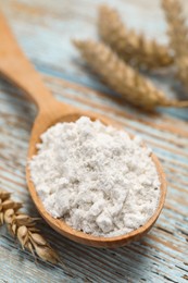 Photo of Spoon of wheat flour on light wooden table, closeup