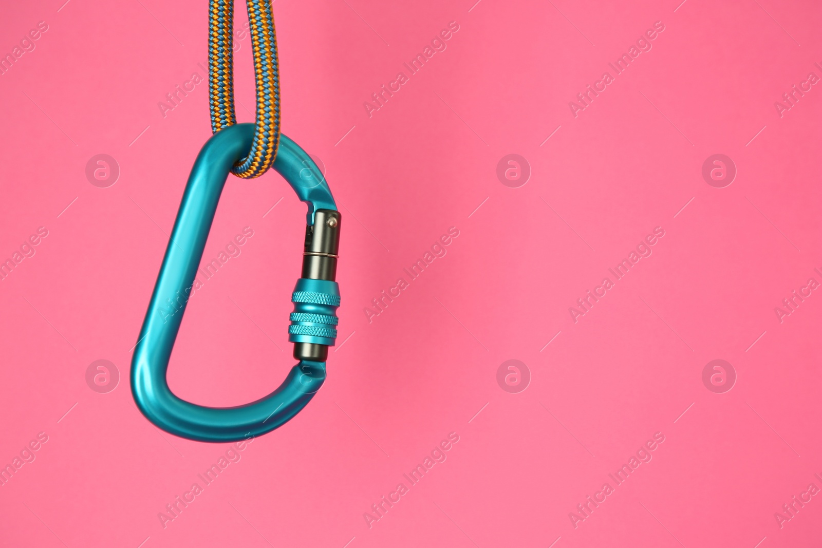 Photo of One metal carabiner hanging on rope against bright pink background. Space for text