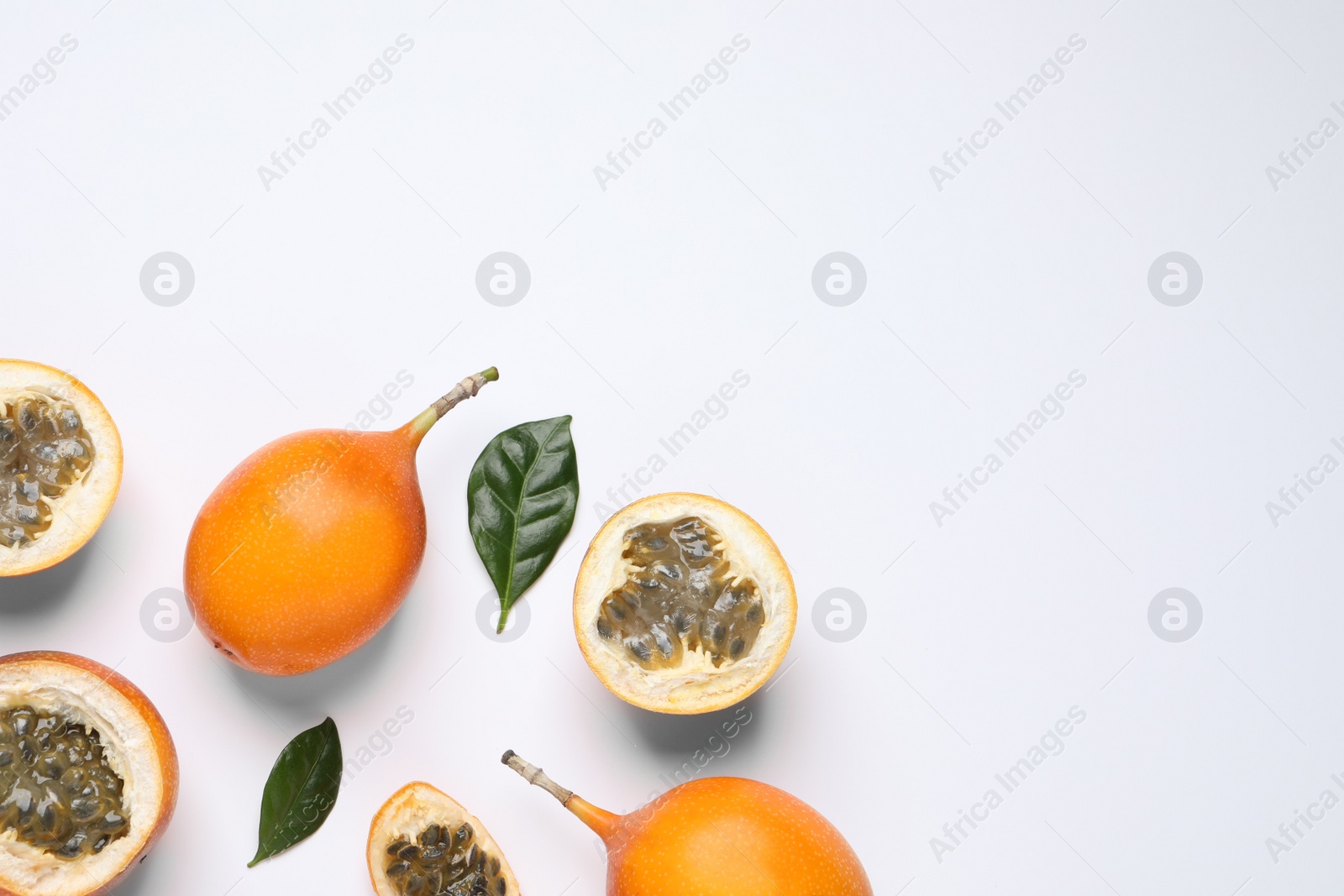 Photo of Delicious ripe granadillas with leaves on white background, flat lay. Space for text