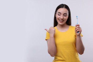 Photo of Happy young woman holding plastic toothbrush and pointing on white background, space for text