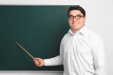 Portrait of male teacher with pointer near chalkboard in classroom