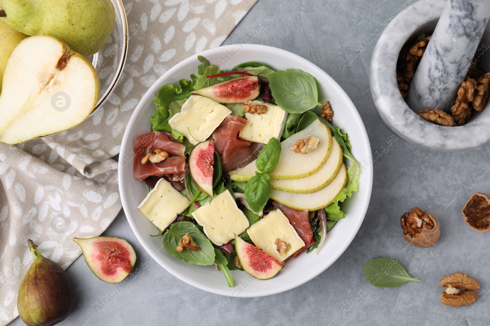 Photo of Tasty salad with brie cheese, prosciutto, pear and figs on grey table, flat lay