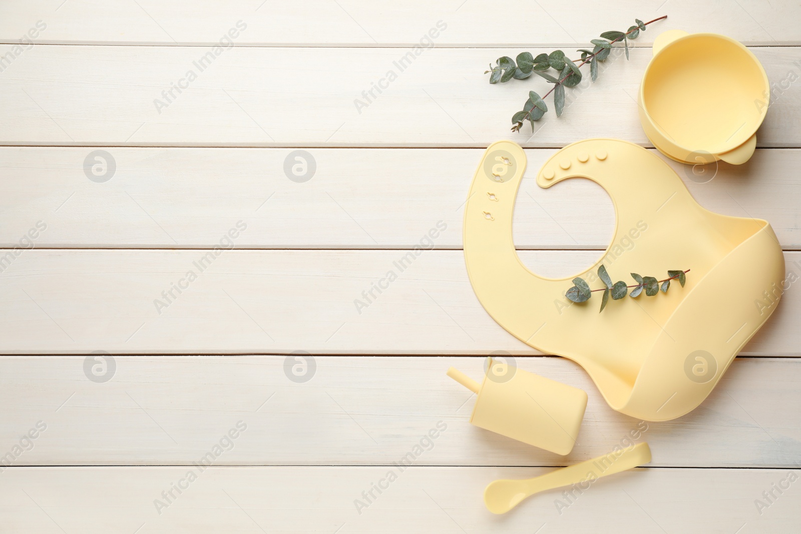 Photo of Flat lay composition with silicone baby bib and plastic dishware on white wooden background. Space for text