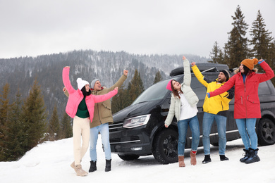 Photo of Happy people jumping near car on snowy road. Winter vacation
