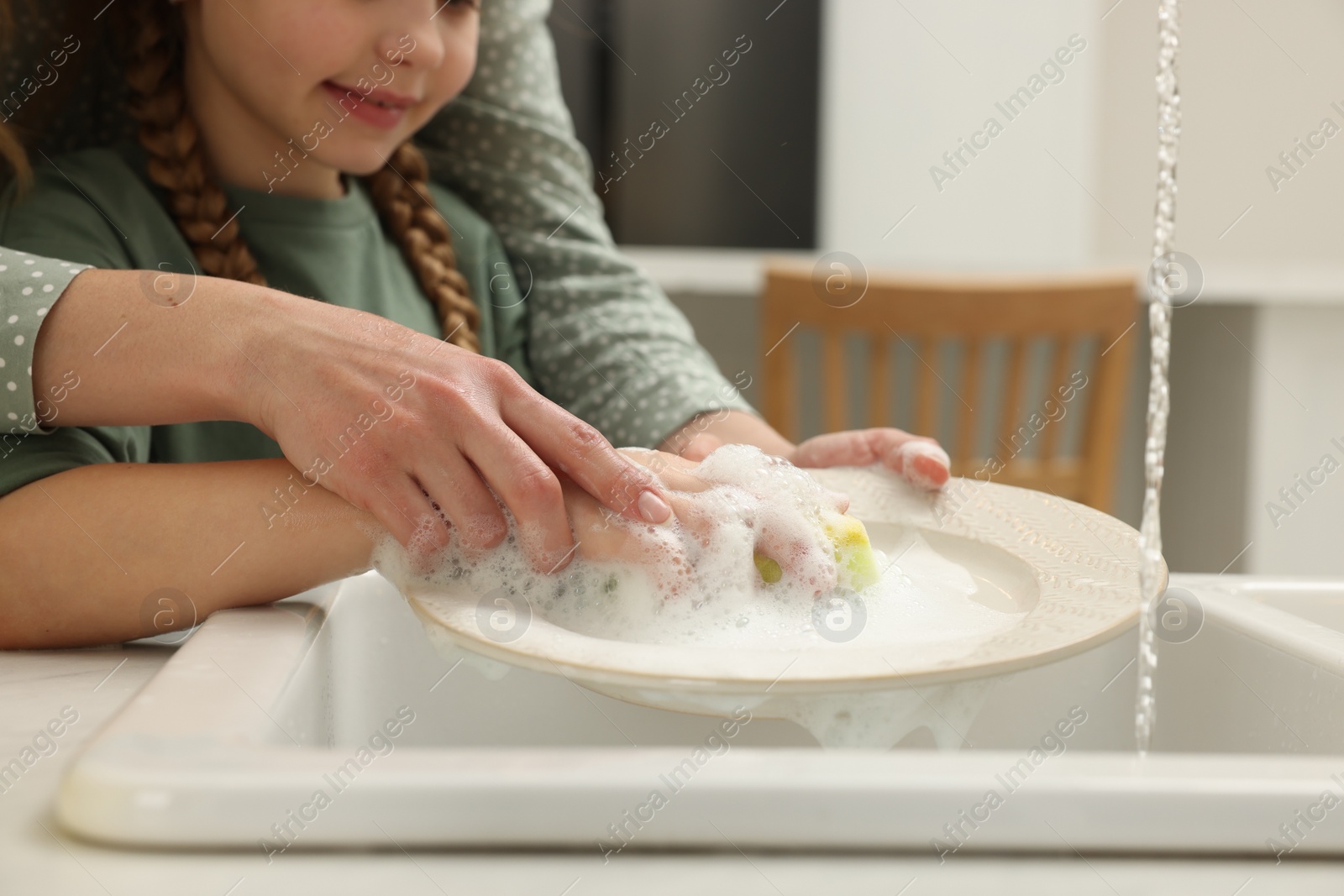 Photo of Mother and daughter washing plate above sink indoors, closeup