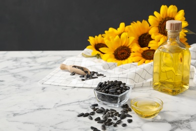 Photo of Sunflower oil and seeds on white marble table, space for text