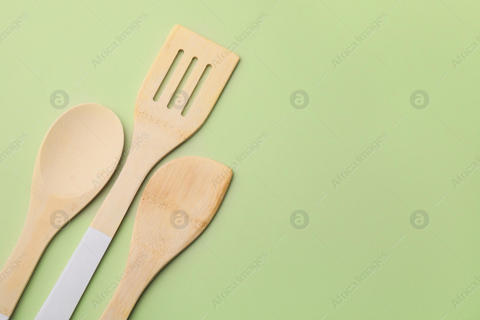 Photo of Wooden kitchen utensils on light olive background, flat lay. Space for text