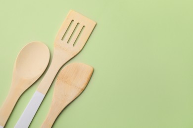 Photo of Wooden kitchen utensils on light olive background, flat lay. Space for text