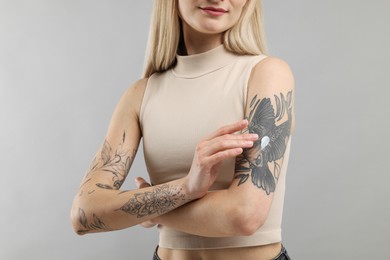 Photo of Tattooed woman applying cream onto her arm on gray background, closeup